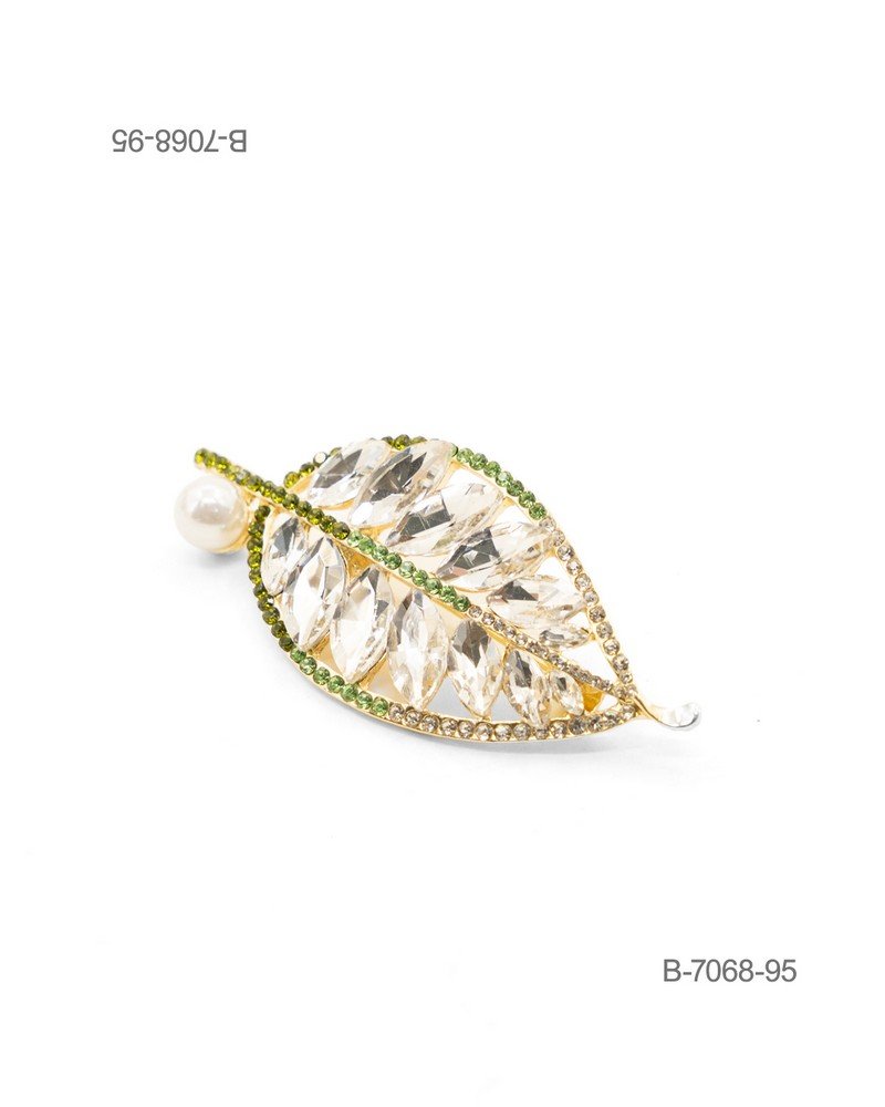 Prendedor de diseño elegante en color dorado, con forma de hoja ornamentada con grandes cristales facetados transparentes, bordes de pedrería verde y transparente, y una perla decorativa en el tallo B7068