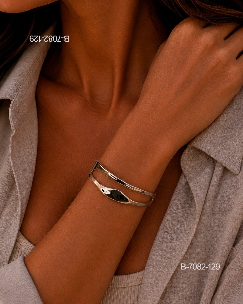 Pulsera rígida o brazalete de diseño elegante en color plateado o metalizado, compuesto por una estructura de doble banda abierta con curvas orgánicas y un acabado brillante B7082